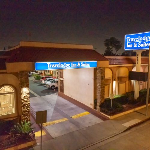 The image shows the entrance of a Travelodge Inn & Suites at night, with lit signage and a view of the parking area.