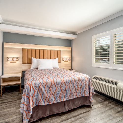 A cozy bedroom with a bed, nightstands, a window with shutters, and an air conditioning unit under the window.