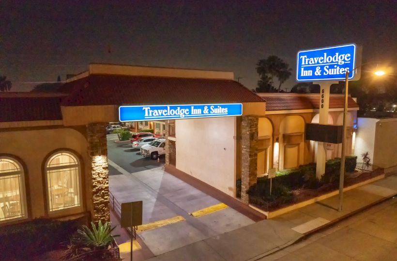 The image shows a Travelodge Inn & Suites at night, with illuminated signage and an entrance driveway.
